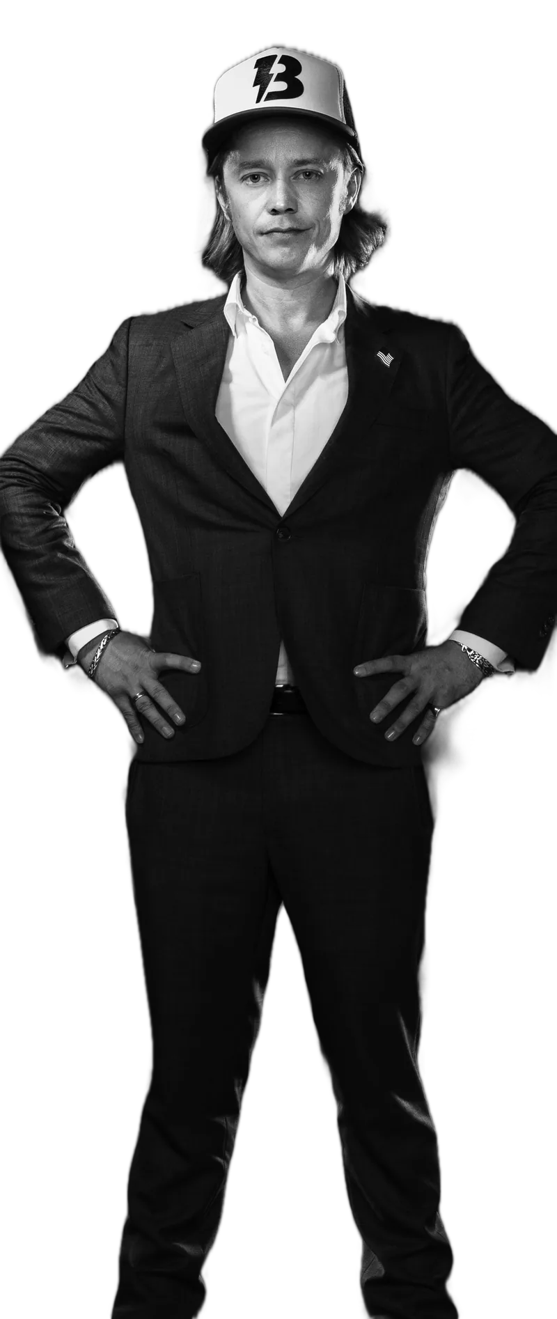Brock Pierce standing, hands on hips, in a suit and a cap with a lightning-bolt B, in black and white